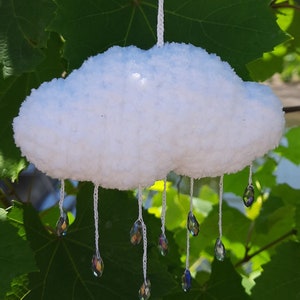 Puede incluir: M&oacute;vil de nube blanca y esponjosa hecho a mano con l&aacute;grimas de cristal colgantes. La nube est&aacute; hecha de un material suave y texturizado, y los cristales iridiscentes est&aacute;n suspendidos por hilos blancos. El fondo presenta hojas verdes.