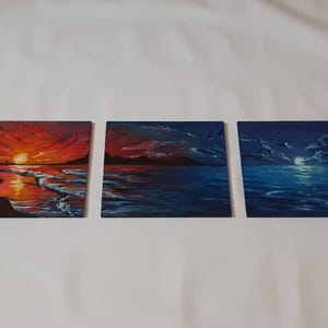 May include: Three small paintings depicting a seascape at different times of day. The first painting shows a sunset over the ocean with a red and orange sky. The second painting shows a twilight scene with a blue sky and a few clouds. The third painting shows a night scene with a dark blue sky and a full moon.