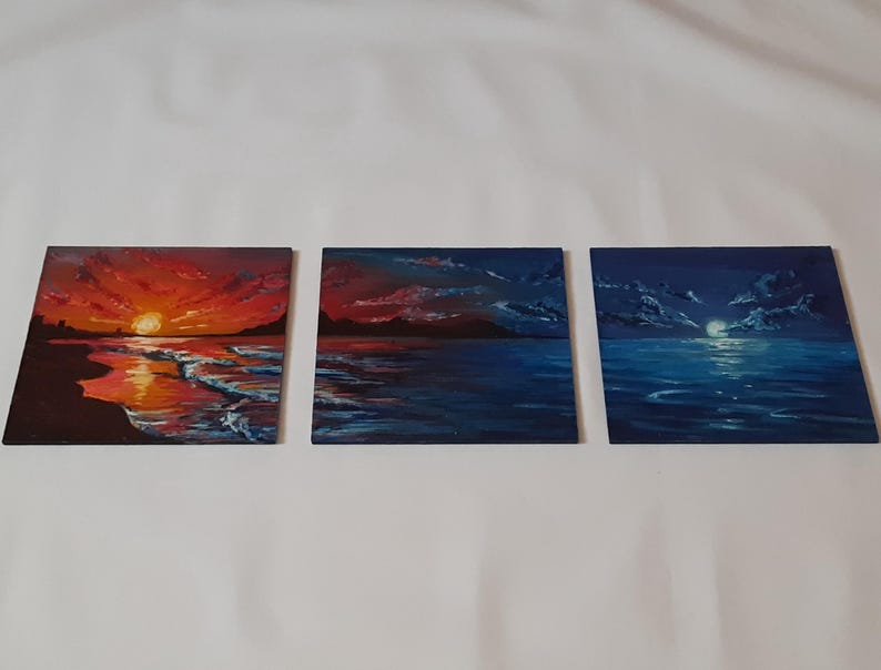 May include: Three small paintings depicting a seascape at different times of day. The first painting shows a sunset over the ocean with a red and orange sky. The second painting shows a twilight scene with a blue sky and a few clouds. The third painting shows a night scene with a dark blue sky and a full moon.