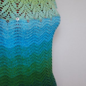 May include: A crocheted top with a green, blue, and turquoise ombre pattern. The top has a scalloped hem and is decorated with small, shiny embellishments.