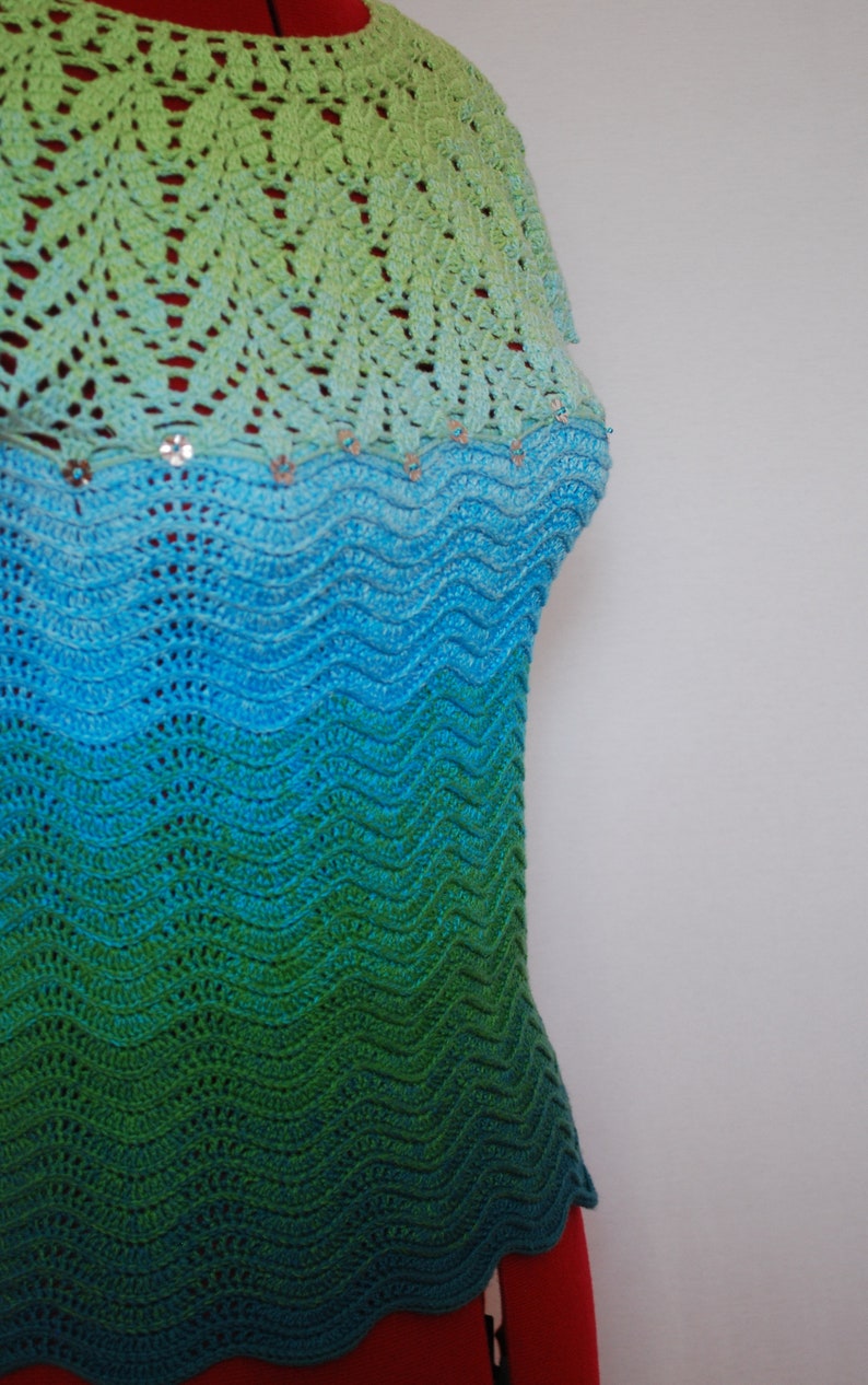 May include: A crocheted top with a green, blue, and turquoise ombre pattern. The top has a scalloped hem and is decorated with small, shiny embellishments.