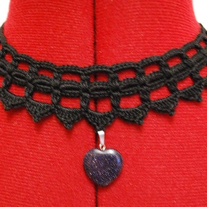 May include: A black crocheted choker necklace with a heart-shaped pendant. The pendant is made of a dark blue stone with a sparkly finish.