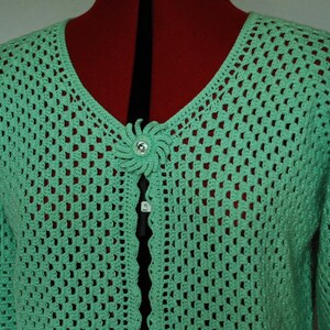 May include: A light green crocheted cardigan with a decorative flower button.