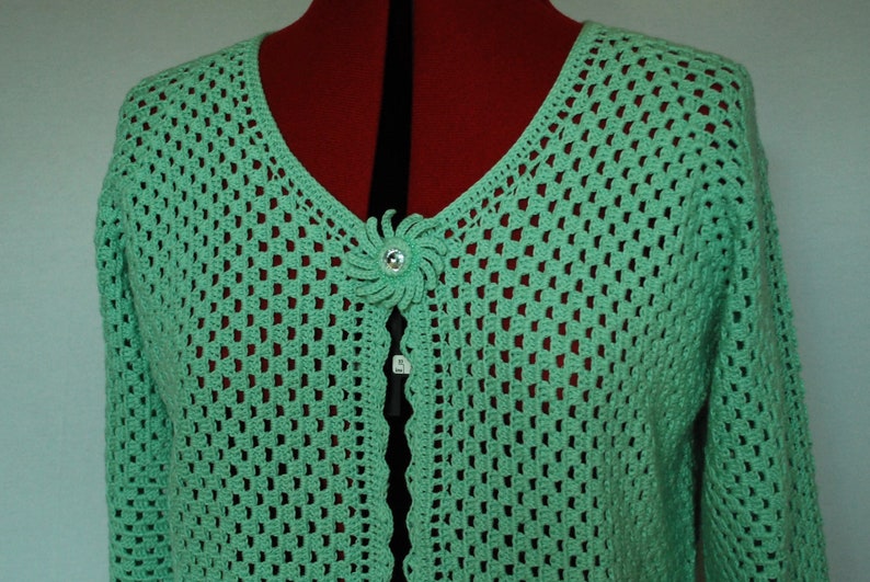 May include: A light green crocheted cardigan with a decorative flower button.