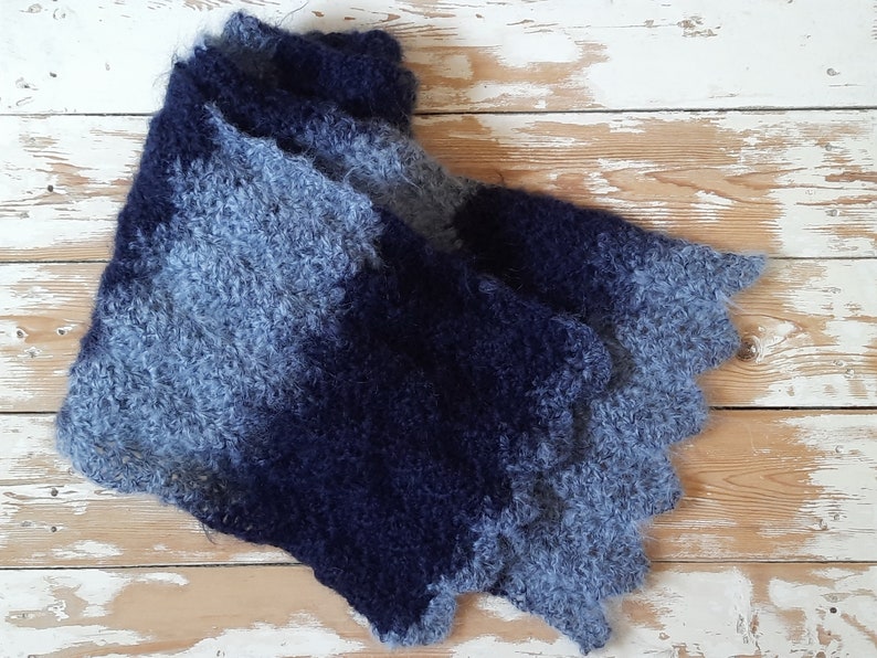 May include: A blue and gray knitted scarf with a fuzzy texture. The scarf is folded in half and laid on a white wooden surface.