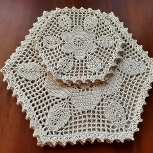 May include: Two crocheted doilies in a beige color, one slightly larger than the other, with intricate floral patterns. The doilies are layered on top of each other, creating a delicate and elegant design.