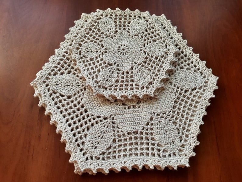 May include: Two crocheted doilies in a beige color, one slightly larger than the other, with intricate floral patterns. The doilies are layered on top of each other, creating a delicate and elegant design.
