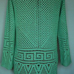 May include: A green crocheted sweater with a geometric pattern. The sweater has long sleeves and a loose fit.