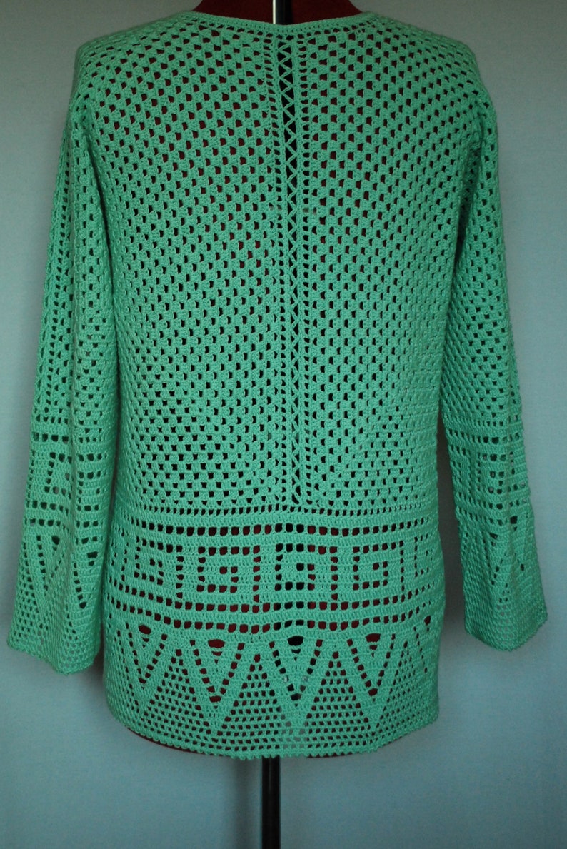 May include: A green crocheted sweater with a geometric pattern. The sweater has long sleeves and a loose fit.
