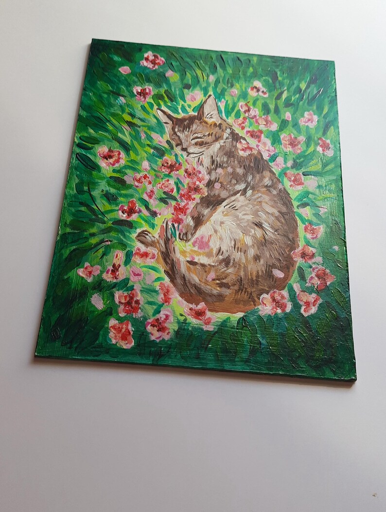 Puede incluir: Una pintura de un gato atigrado marr&oacute;n durmiendo en un campo de flores rosas. El gato est&aacute; enroscado en una bola con los ojos cerrados. Las flores est&aacute;n en flor y el fondo es un verde exuberante.