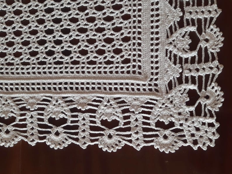K&ouml;nnte beinhalten: Wei&szlig;e H&auml;keltischdecke mit quadratischem Mittelteil und einem gewellten Rand. Die Tischdecke hat ein zartes Blumenmuster.