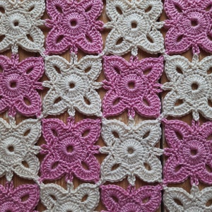 May include: A crocheted square pattern with alternating pink and cream coloured squares. The squares are made with a simple flower design.