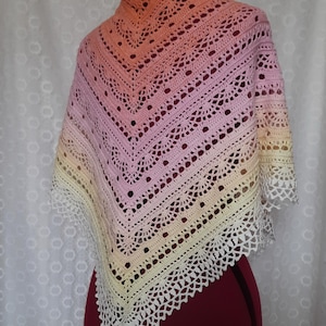 May include: A handmade crochet shawl in a gradient of colors, transitioning from peach to pink, then to yellow, and finally to white. The shawl features an openwork design with a scalloped edge, displayed on a mannequin.