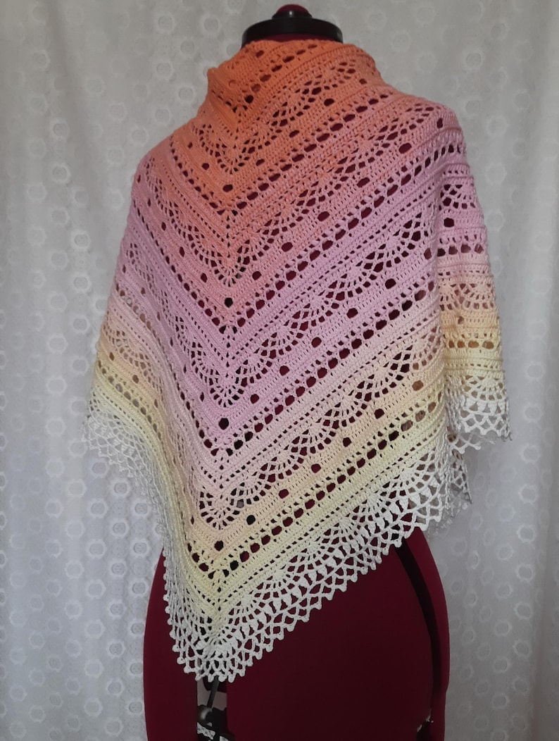 May include: A handmade crochet shawl in a gradient of colors, transitioning from peach to pink, then to yellow, and finally to white. The shawl features an openwork design with a scalloped edge, displayed on a mannequin.