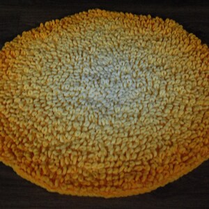 May include: A round, yellow and white bath mat with a gradient pattern. The mat is made of a soft, fluffy material.