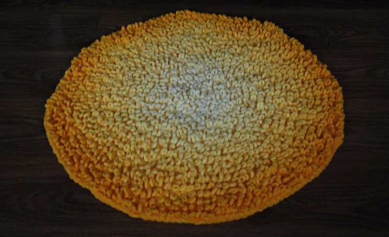 May include: A round, yellow and white bath mat with a gradient pattern. The mat is made of a soft, fluffy material.