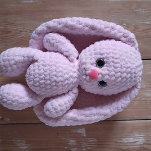 K&ouml;nnte beinhalten: Ein weiches, rosa geh&auml;keltes Hasenspielzeug mit gro&szlig;en schwarzen Augen und einer rosa Nase. Der Hase liegt auf dem R&uuml;cken mit ausgebreiteten Beinen und Ohren.