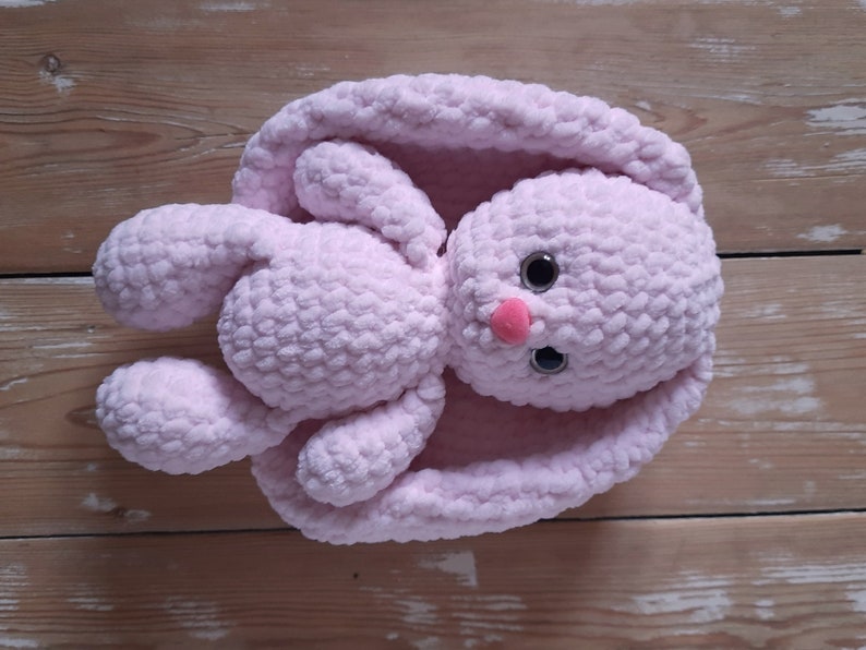 K&ouml;nnte beinhalten: Ein weiches, rosa geh&auml;keltes Hasenspielzeug mit gro&szlig;en schwarzen Augen und einer rosa Nase. Der Hase liegt auf dem R&uuml;cken mit ausgebreiteten Beinen und Ohren.