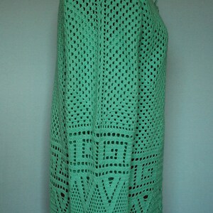 May include: A green crocheted cardigan with a geometric pattern. The cardigan has a V-neck and long sleeves.