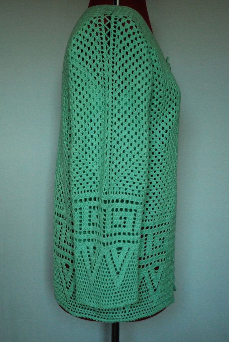 May include: A green crocheted cardigan with a geometric pattern. The cardigan has a V-neck and long sleeves.