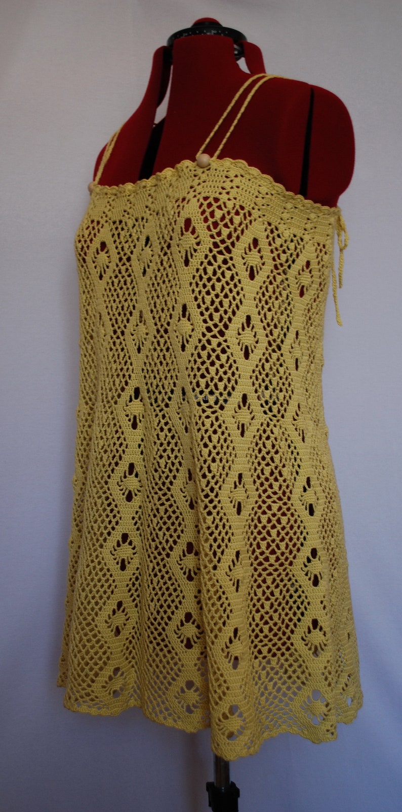May include: A yellow crochet dress with a delicate pattern. The dress has a halter neckline and a loose fit.