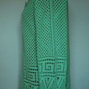 May include: A green crocheted cardigan with a geometric pattern. The cardigan has long sleeves and a V-neck.