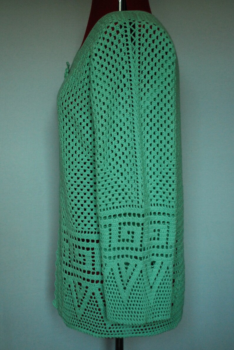 May include: A green crocheted cardigan with a geometric pattern. The cardigan has long sleeves and a V-neck.