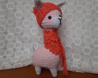 Könnte beinhalten: Ein rosa gehäkeltes Lama, das eine leuchtend orangefarbene gehäkelte Mütze und einen Schal trägt. Das Lama hat weiße Ohren und eine weiße Nase.