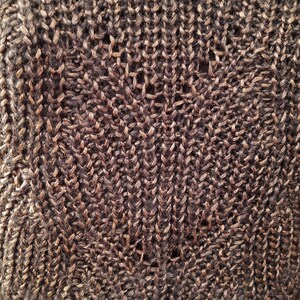 May include: Close-up of a brown knitted fabric with a textured pattern. The fabric has a subtle sheen and a soft, fuzzy texture.