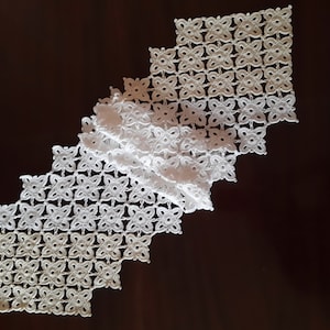 May include: White crocheted table runner with a diamond shape and a delicate floral pattern.