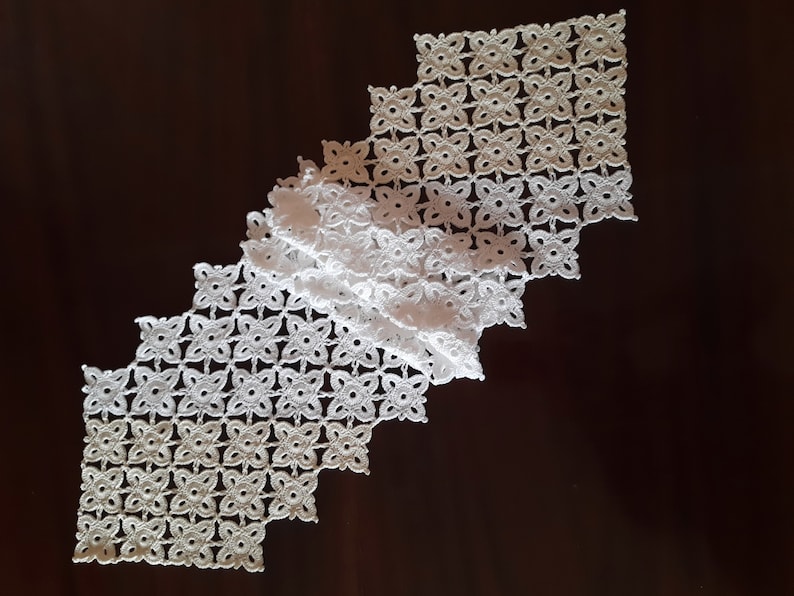 May include: White crocheted table runner with a diamond shape and a delicate floral pattern.