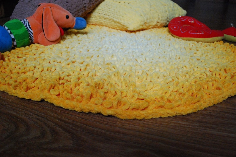 May include: A yellow and white crocheted rug with a gradient pattern. The rug is round and has a soft, fluffy texture.