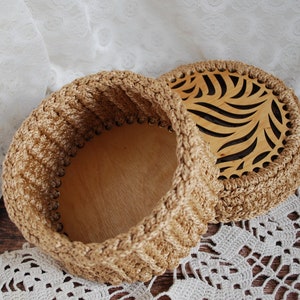Pu&ograve; includere: Una scatola di immagazzinaggio rotonda in crochet con un coperchio in legno con un design a foglia ritagliata. La scatola &egrave; beige e il coperchio &egrave; in legno naturale.