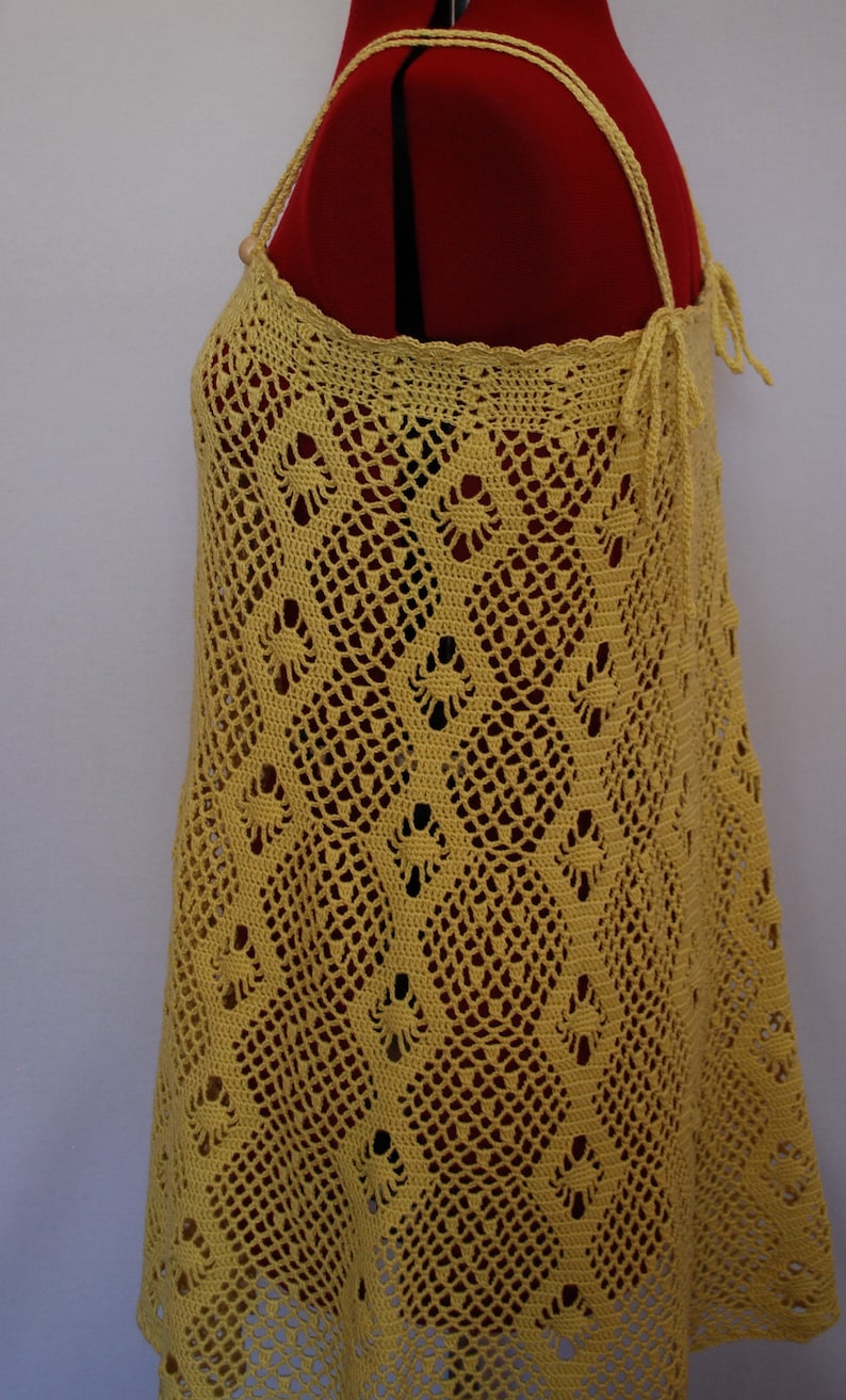 May include: A yellow crochet top with a delicate pattern. The top has a halter style with thin straps and a tie at the back.