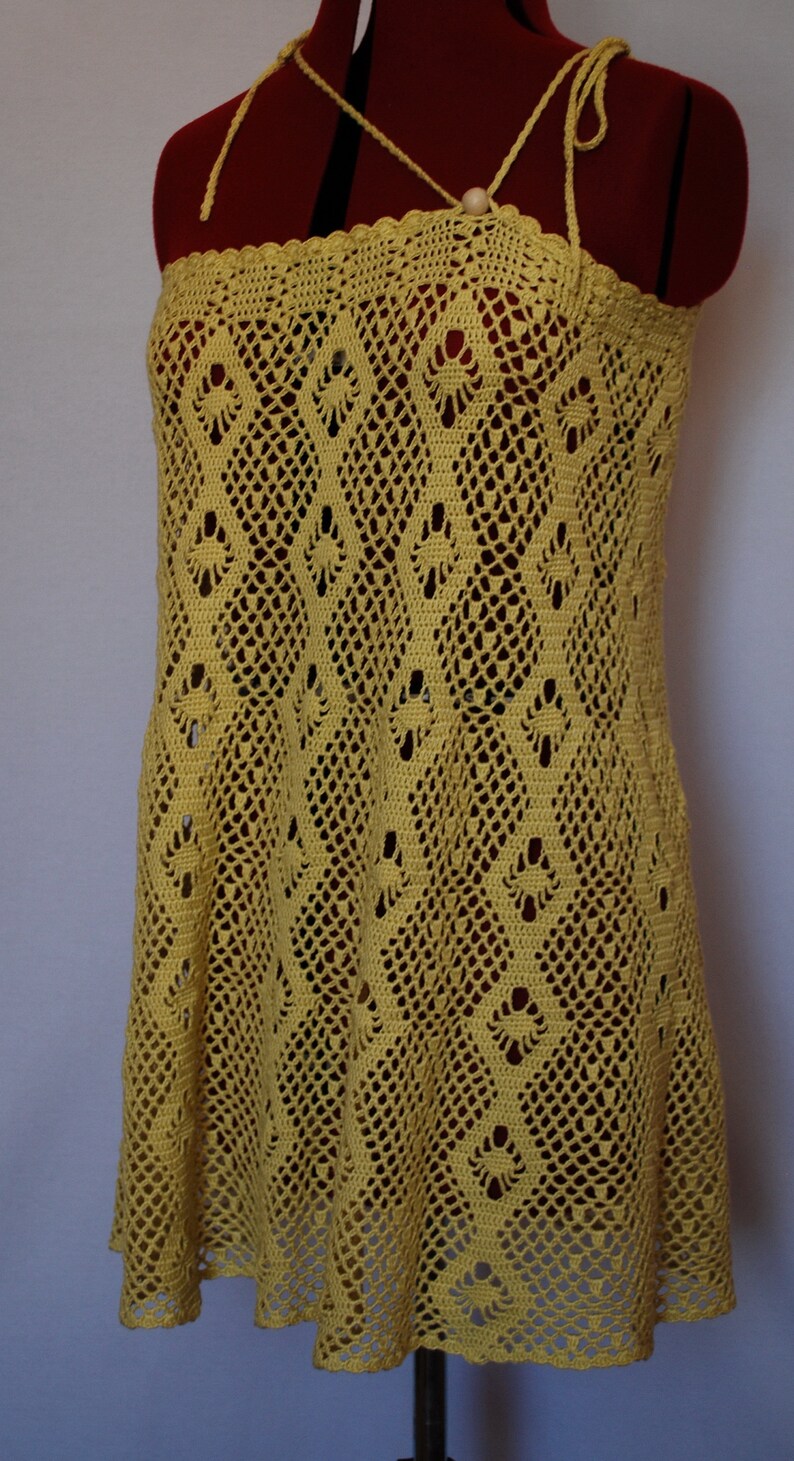 May include: A yellow crochet dress with a delicate, lacy pattern. The dress has a scoop neck and thin straps.