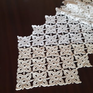 May include: White crocheted table runner with a delicate floral pattern. The runner is made of a fine thread and has a scalloped edge.