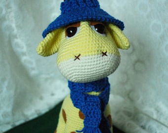 Girafa de crochê em amigurumi: bichinho de pelúcia com chapéu e cachecol azuis.