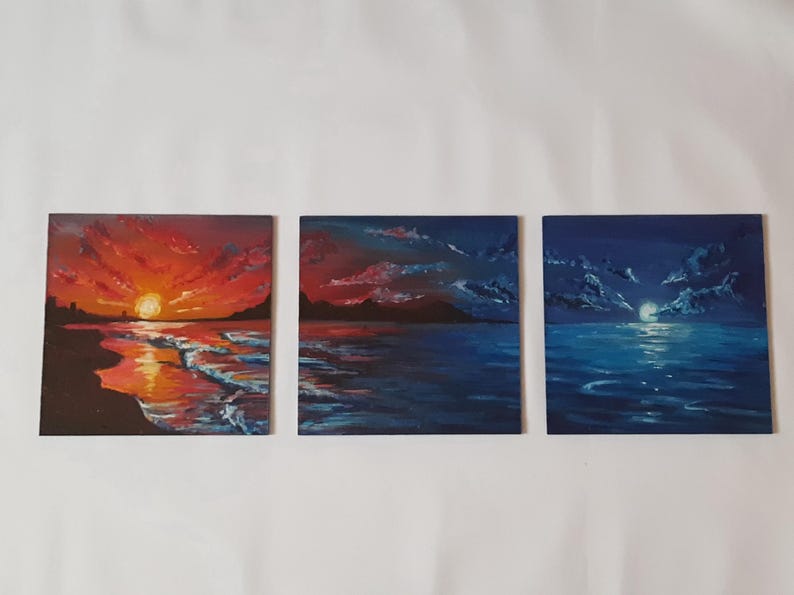 May include: Three small paintings depicting seascapes. The first painting shows a sunset over the ocean with a red and orange sky. The second painting shows a blue sky with clouds and a dark silhouette of a coastline. The third painting shows a dark blue sky with a full moon and a dark blue ocean.