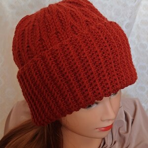 May include: A red crocheted beanie hat with a ribbed texture. The hat is worn on a mannequin head.