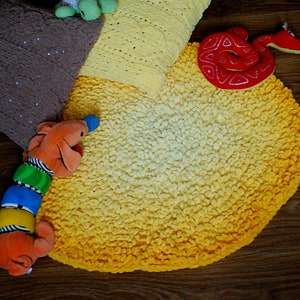 May include: A yellow and white crocheted round rug with a brown and white crocheted pillow and a red snake toy on top.