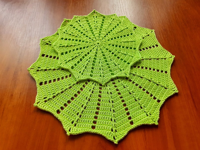 May include: Three green crocheted doilies with a starburst pattern. The doilies are layered on top of each other.