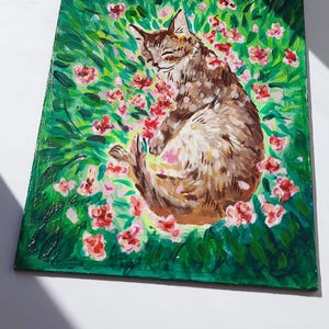 Puede incluir: Una pintura de un gato atigrado marr&oacute;n durmiendo en un campo de flores rosas. El gato est&aacute; rodeado de hierba verde y hojas.