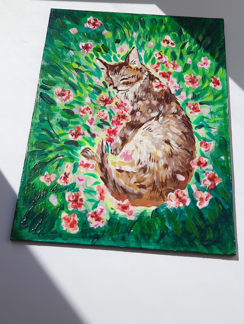 Puede incluir: Una pintura de un gato atigrado marr&oacute;n durmiendo en un campo de flores rosas. El gato est&aacute; rodeado de hierba verde y hojas.