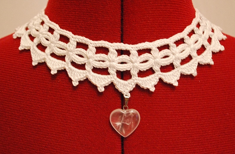 May include: White crocheted lace choker necklace with a clear heart-shaped crystal pendant.