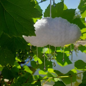 Puede incluir: Decoraci&oacute;n de nube blanca y esponjosa con gotas de cristal colgantes. La nube est&aacute; suspendida por un hilo blanco, sobre un fondo de hojas verdes y luz solar. Ideal para la decoraci&oacute;n del hogar.