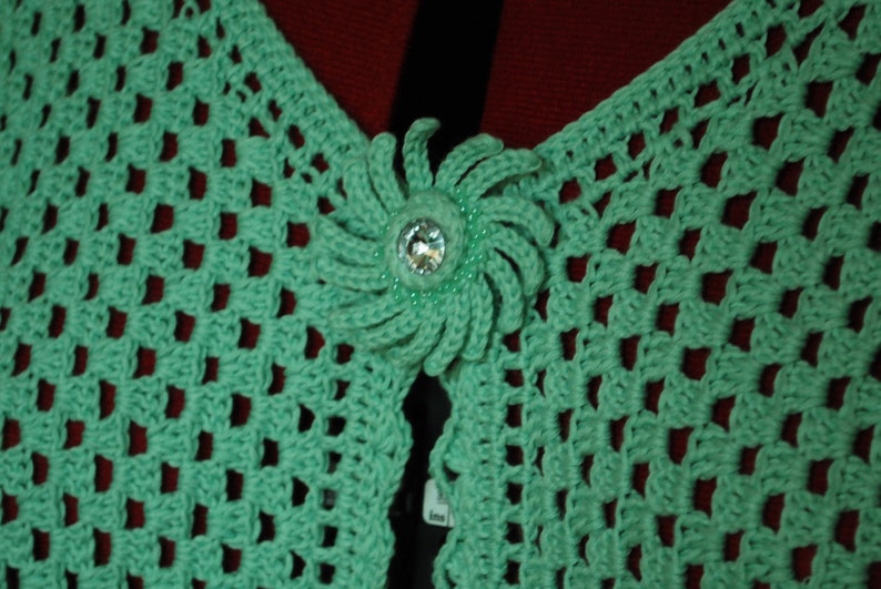 May include: A green crocheted shawl with a decorative flower-shaped button in the centre.