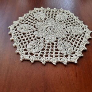 May include: A white crocheted doily with a delicate floral design. The doily is circular and has a scalloped edge.