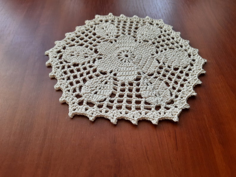 May include: A white crocheted doily with a delicate floral design. The doily is circular and has a scalloped edge.