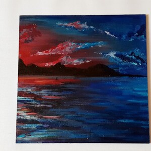 May include: A painting of a sunset over a body of water. The sky is a vibrant red and orange, with dark blue clouds. The water is a deep blue, with reflections of the sunset on the surface.