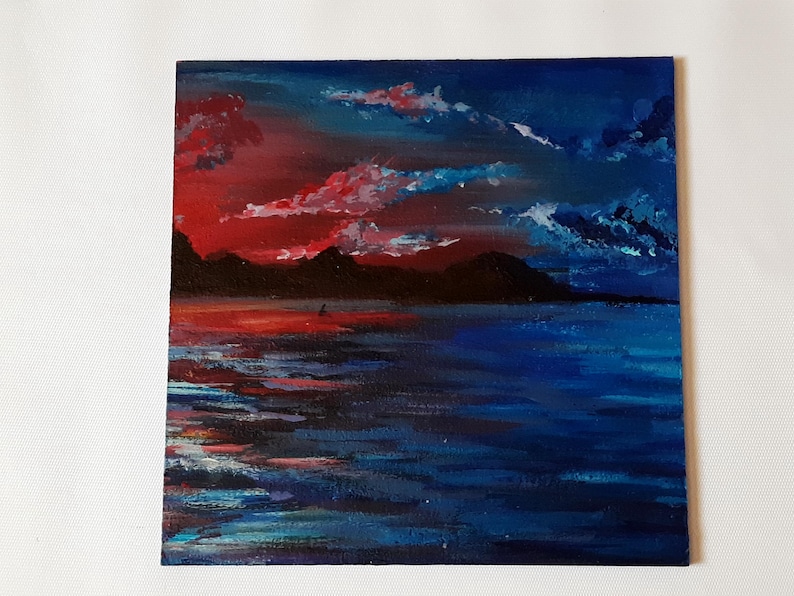 May include: A painting of a sunset over a body of water. The sky is a vibrant red and orange, with dark blue clouds. The water is a deep blue, with reflections of the sunset on the surface.